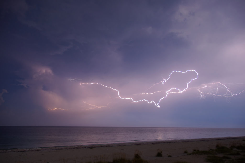 lightning bolts stretching across clouds over a beach